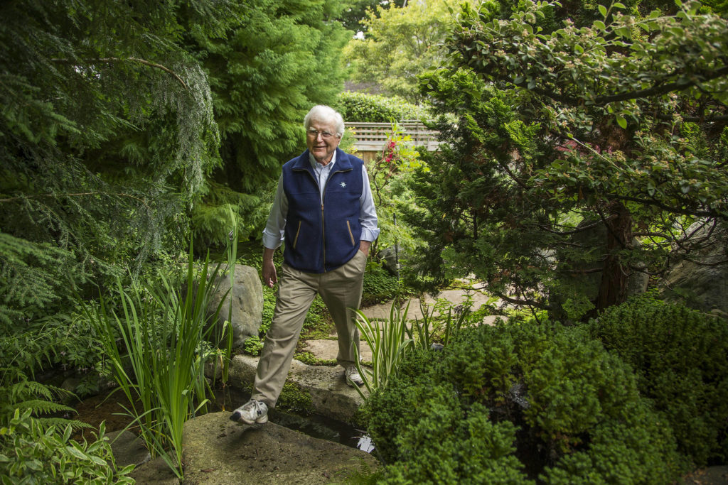 Bill Taylor steps over a water feature in his garden in Edmonds. (Andy Bronson / The Herald)
