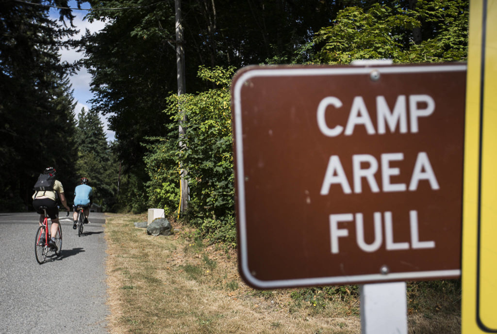 Ben Watanabe and Zachariah Bryan ride into a full campground at Wenberg County Park on Saturday near Stanwood. A weekday bus can deliver campers less than two miles away on Highway 531. (Olivia Vanni / The Herald)
