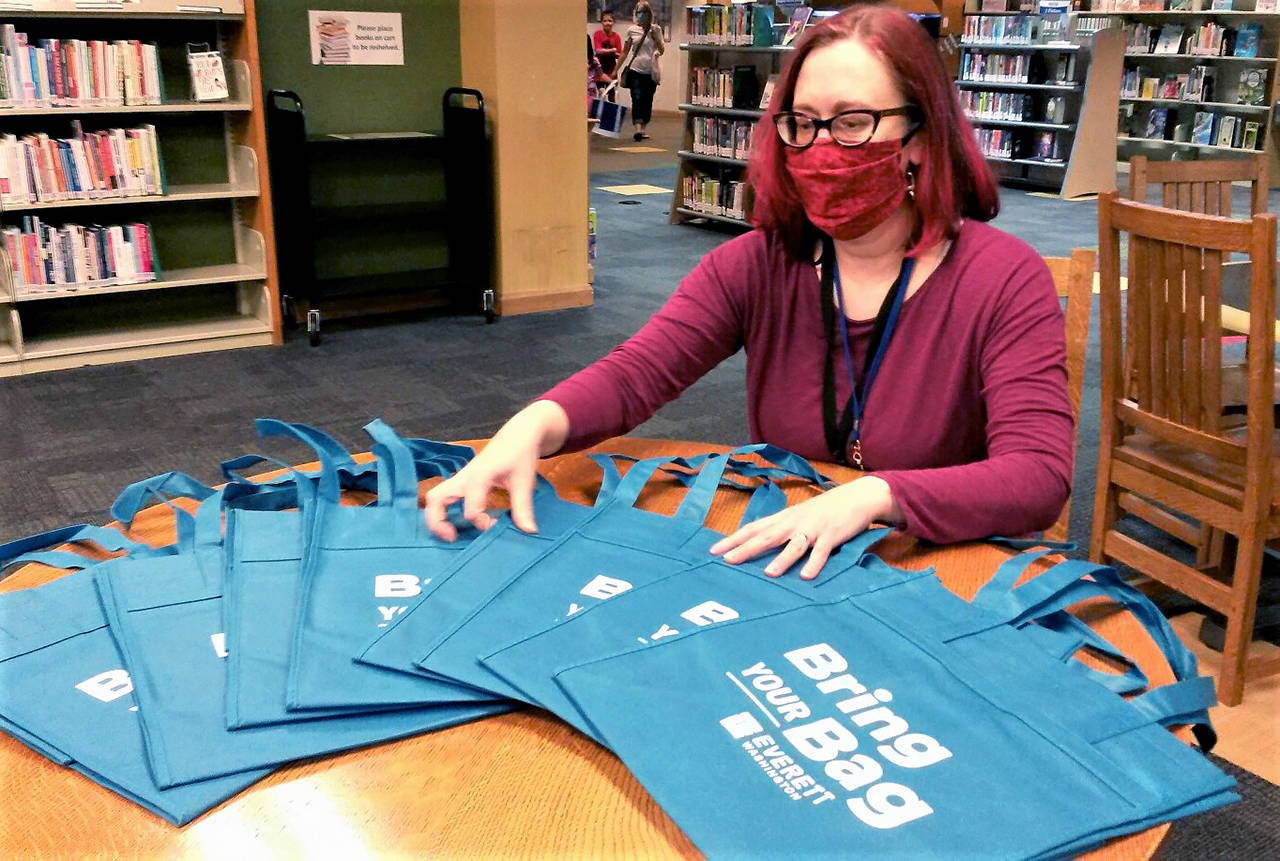 Emily Dagg, assistant director of the Everett Public Library, shows reusable bags the city of Everett is giving out at the downtown library and Evergreen Branch while supplies last. (Julie Muhlstein / The Herald)