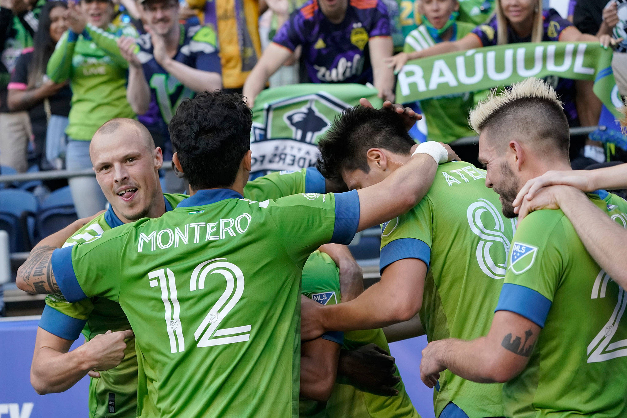 Sounders players, including Brad Smith (left), and Fredy Montero (12), surround forward Raul Ruidiaz (obscured) after Ruidiaz scored a goal against the Dynamo during the second half of an MLS match on July 7, 2021, in Seattle. The Sounders won 2-0. (AP Photo/Ted S. Warren)