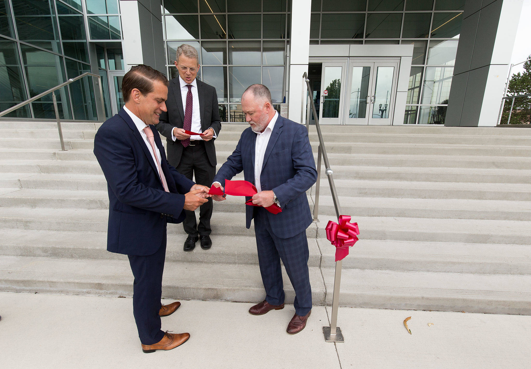 After cutting a section for Snohomish County Superior Court Judge George Appel, Joshua Dugan cuts off a piece of ribbon for Snohomish County Prosecuting Attorney Adam Cornell after the ceremony to mark the completion of the Snohomish County Courthouse remodel and addition project Thursday in Everett. (Andy Bronson / The Herald)