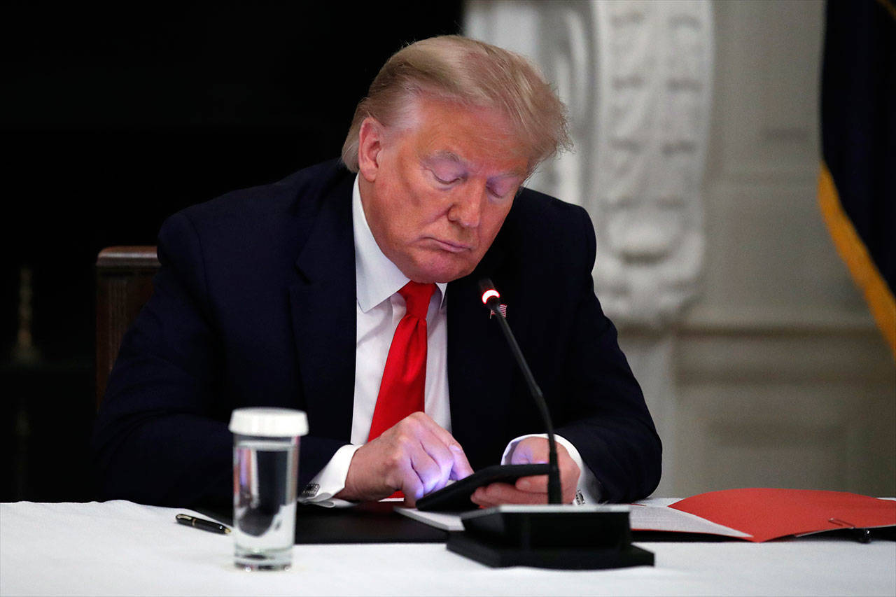 President Trump looks at his phone during a roundtable with governors on the reopening of America’s small businesses, in the State Dining Room of the White House in Washington in June, 2020. Though stripped of his Twitter account for inciting rebellion and barred from Facebook, Trump does have alternative options of much smaller reach. (Alex Brandon/ Associated Press file photo)