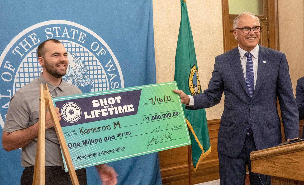 Kameron M. (left) is all smiles at a press conference in Olympia on Friday with Washington Gov. Jay Inslee after accepting a mock check for $1 million, which he won as part of a “Shot of a Lifetime” lottery open to all Washington residents who got the COVID-19 vaccine. (Ellen M. Banner/The Seattle Times via AP)