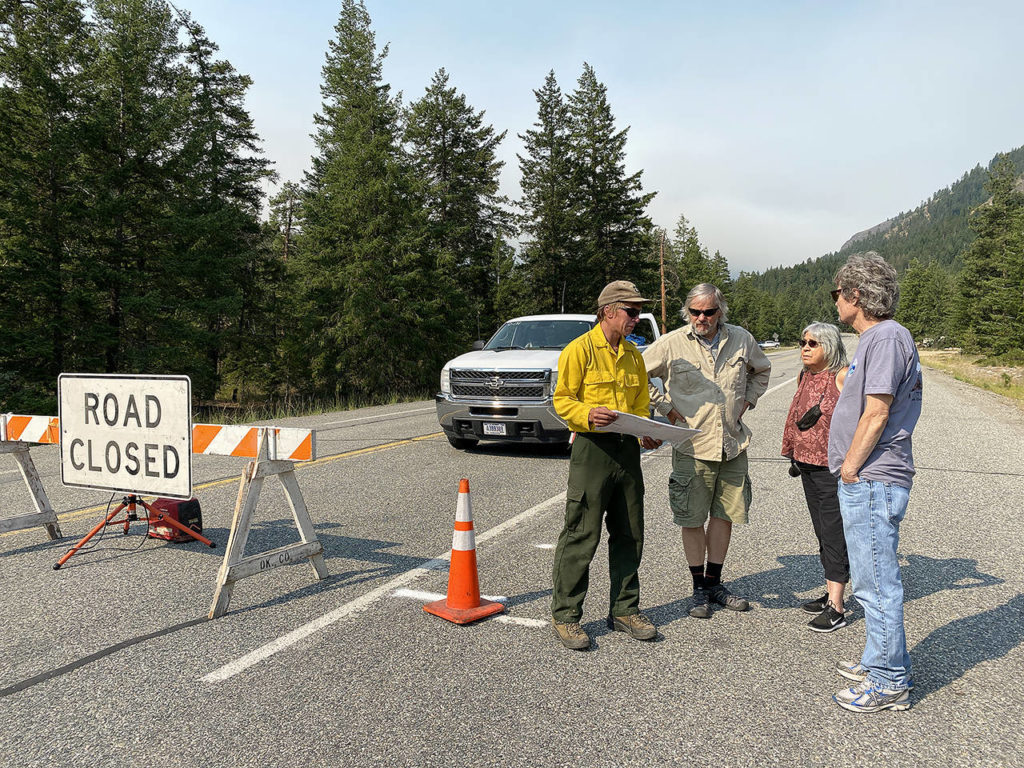Forest Service employee Will Park-Hoffman (left) shows a map of the Cub Creek 2 and Cedar Creek fires to Ray and Sylvia Robertson (center), of Carlton, and Brad Stenberg (right) of Seattle, at the eastern road closure on Highway 20, Sunday near Mazama. (Sue Misao / The Herald)
