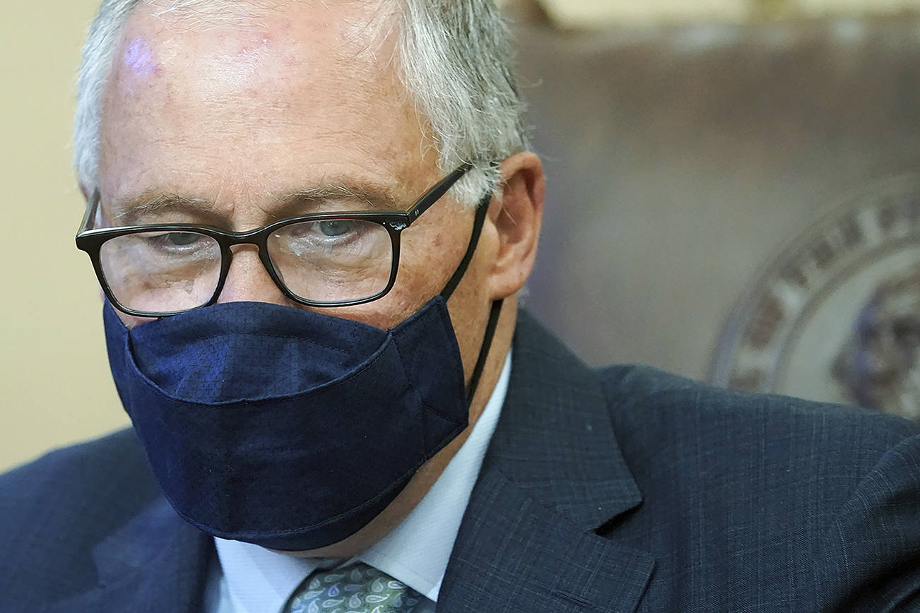 Washington Gov. Jay Inslee looks down at a stack of bills to be signed into law, Wednesday, May 12, 2021, at the Capitol in Olympia, Wash. The measures included a bill that prohibits openly carrying guns and other weapons at the state Capitol and protests statewide. (AP Photo/Ted S. Warren)