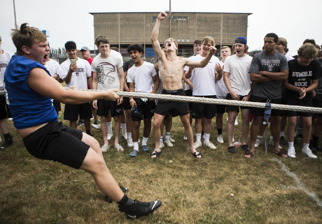 Bothell’s Luka Vincic (left) yells as he pulls the blue flag across the center to win while Mercer Island’s Cole Drayton (center) jumps in celebration during the Cougars Championship Lineman Challenge at Lakewood High School on July 31 in Arlington. (Olivia Vanni / The Herald)