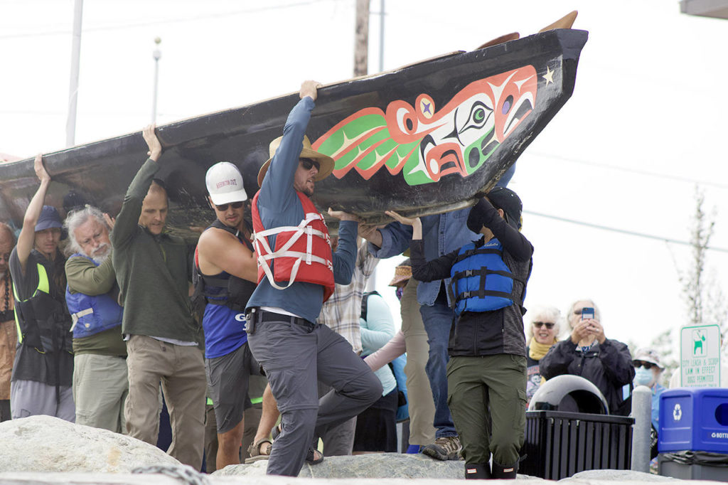 Members of the Blue Heron Canoe Family lift the Willapa Spirit over rocks in front of the Edmonds Waterfront Center on Monday morning. (Isabella Breda / The Herald)
