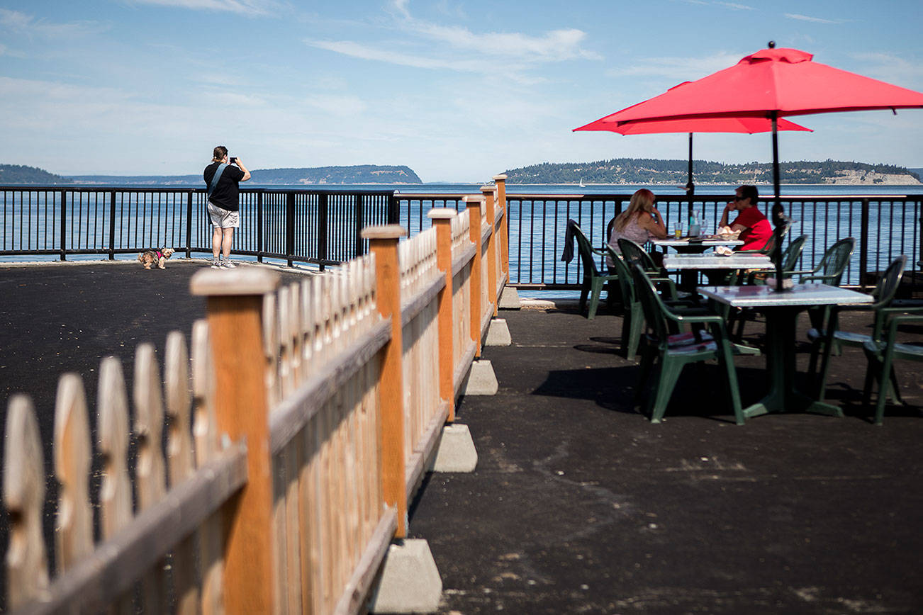 A person takes a photograph of the water from the new parklet while people dine at the new table additions at the parklet for Ivar's on Thursday, Aug. 5, 2021 in Mukilteo, Wash. (Olivia Vanni / The Herald)