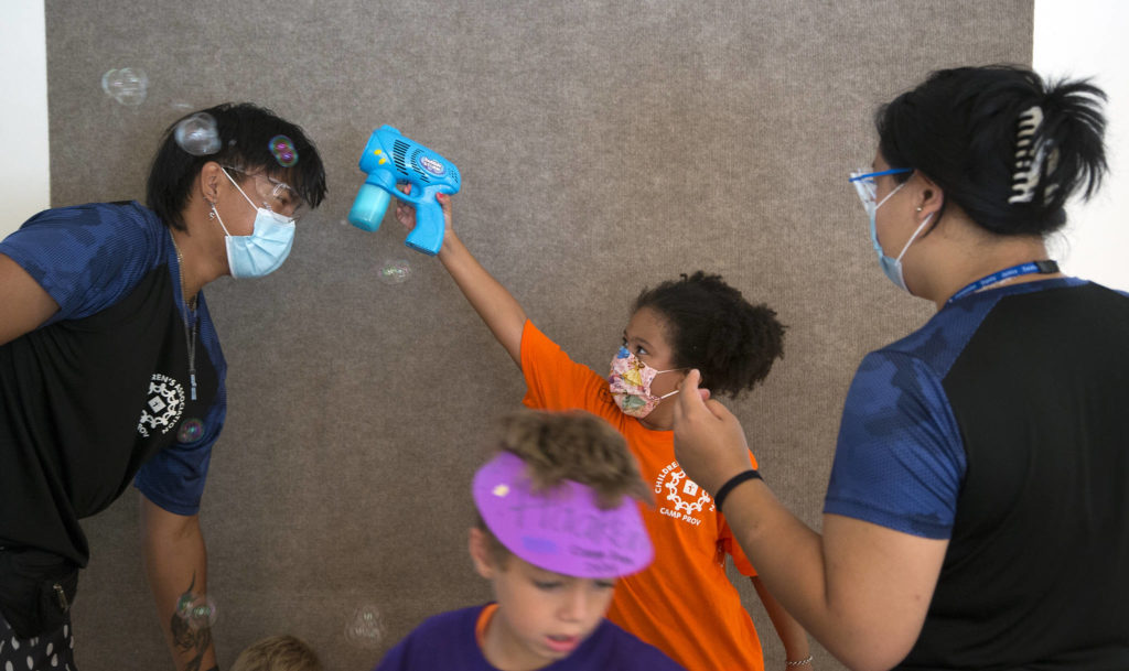 Ellison Lombard tries to get soap bubbles to land on Sage Oliveria’s head during craft time of Camp Prov in Everett. (Andy Bronson / The Herald) 
