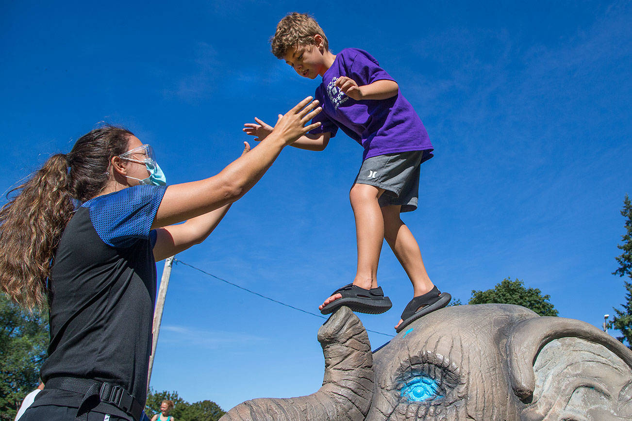 Haaken Williams, 6, balances on the nose of an elephant sculpture at Forest Park as Camp Prov unit leader Megan Pfohl reaches out to him during a playground break on Wednesday, Aug. 11, 2021 in Everett, Washington. Camp Prov is an integrated day camp for children with special needs and their siblings. (Andy Bronson / The Herald)