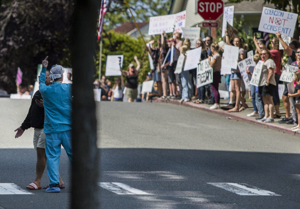 A Providence employee in scrubs reacts to a crowd of vaccine-mandate opponents outside Providence Regional Medical Center Everett on Wednesday. “Betrayed, hurt and sad,” is how he said he felt seeing people protesting outside the hospital. (Olivia Vanni / The Herald) 
