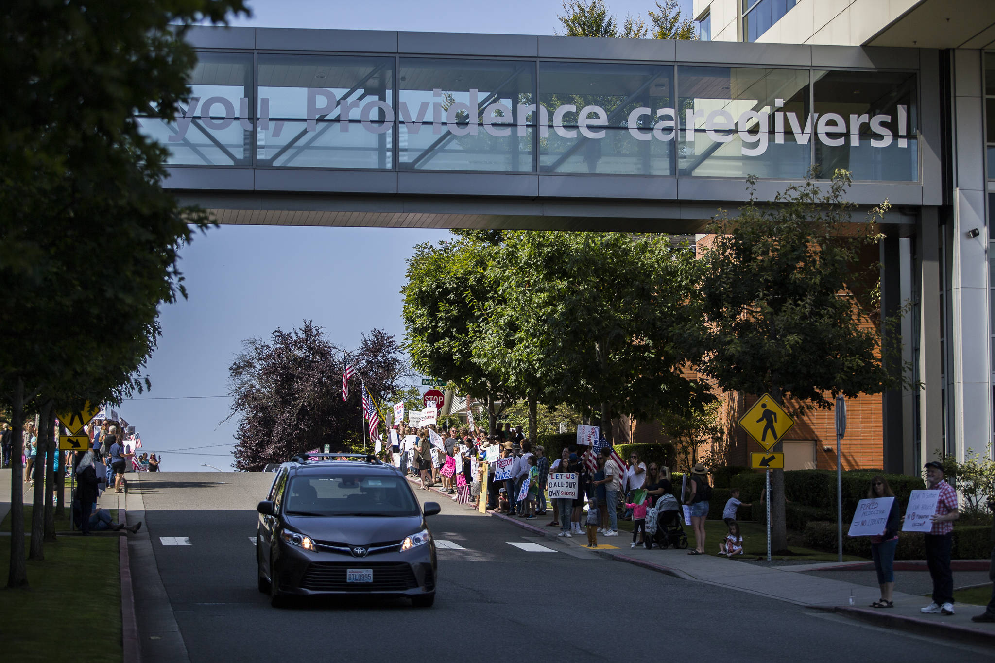 A car drives past people protesting vaccine mandates outside of Providence Regional Medical Center Everett on Aug. 18. (Olivia Vanni / Herald file)
