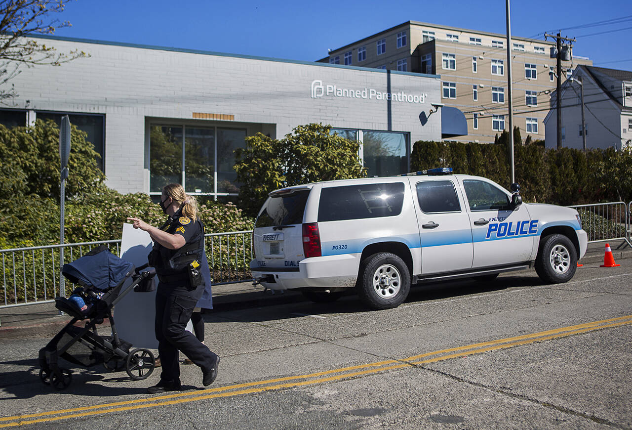 In this April 14 photo, an Everett police officer escorts a demonstrator away from Everett’s Planned Parenthood. At the time, the city prohibited gatherings in an alley and on the sidewalk around the clinic. (Olivia Vanni / Herald file)