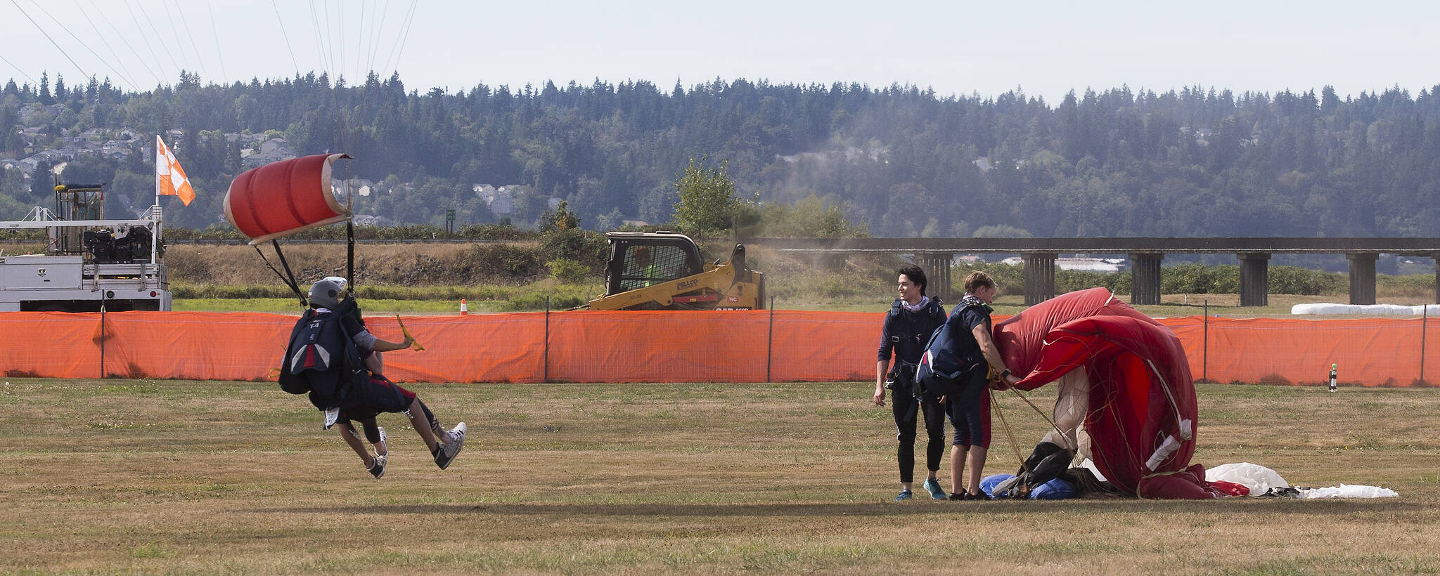 Tandem parachutists with Skydive Snohomish land and gather their canopies at Harvey Field in Snohomish on Thursday while repaving is underway at the nearby asphalt runway. (Andy Bronson / The Herald)
