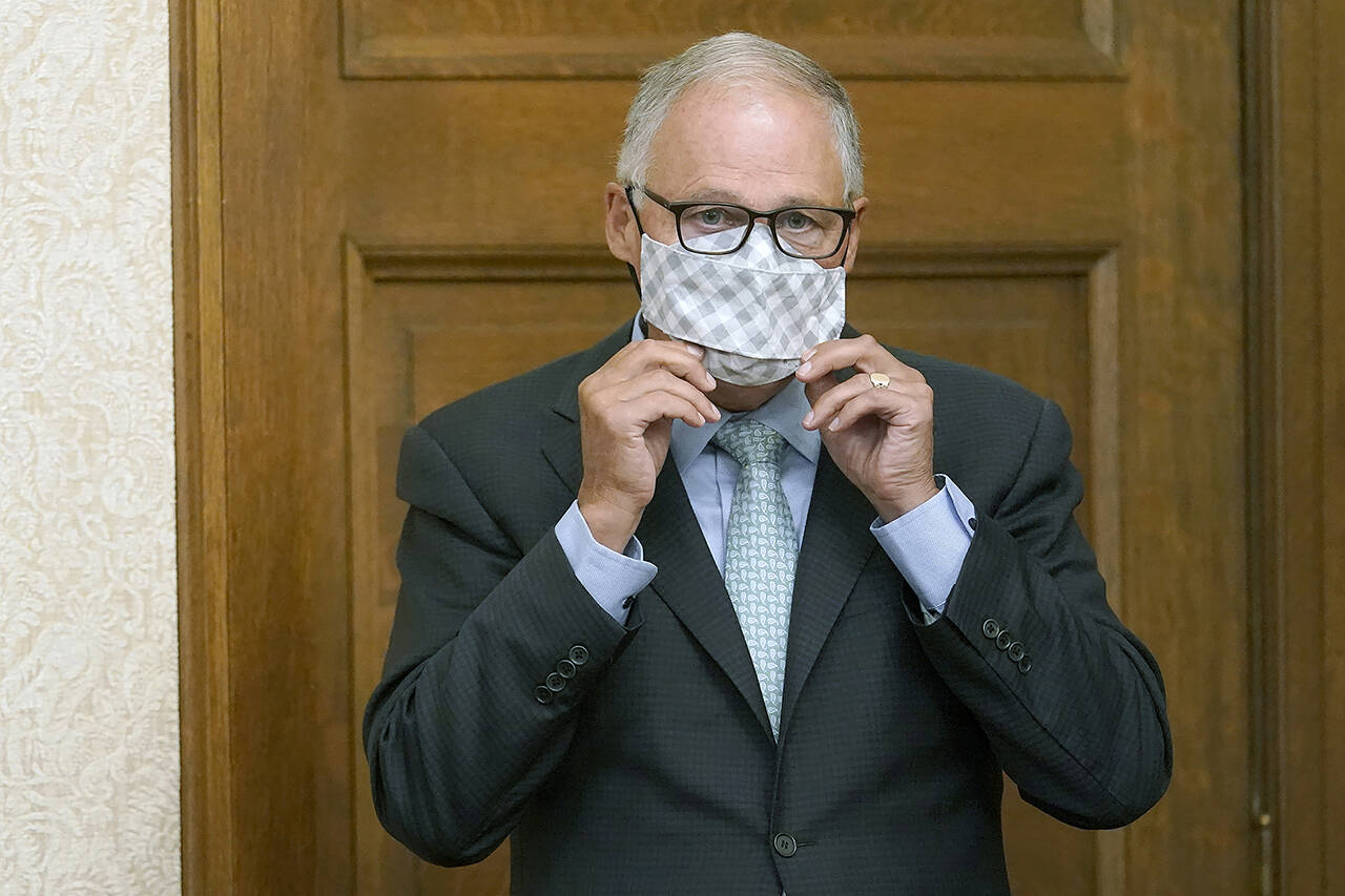 Gov. Jay Inslee puts on a mask after speaking at an Aug. 18 news conference at the Capitol in Olympia. On Thursday, he announced masks will soon be required at large outdoor events across the state. (AP Photo/Ted S. Warren, file)