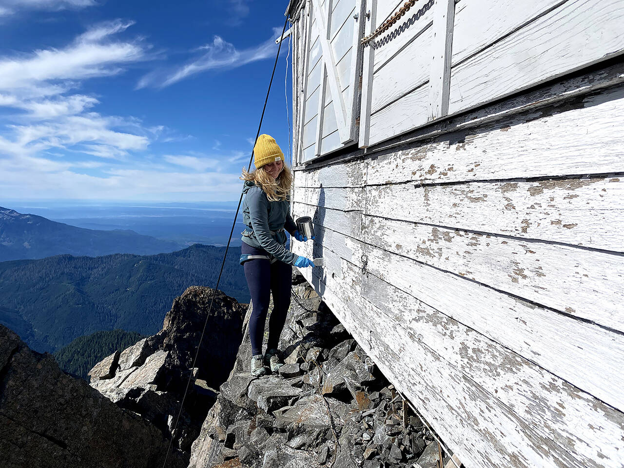 Attached to a harness, Brenna Anderst stands precariously on a ledge as she paints Three Fingers Lookout. (Friends of Three Fingers Lookout)