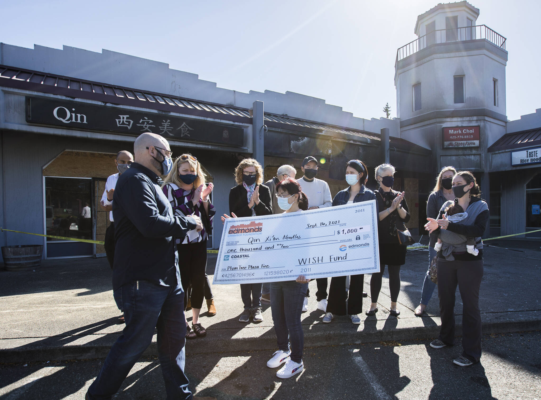 Bufeng Gao, owner of Qin Xi’an Noodles, receives a check Thursday from the Edmonds Chamber Foundation’s Wish Fund outside of her restaurant that was burned in a fire. (Olivia Vanni / The Herald)