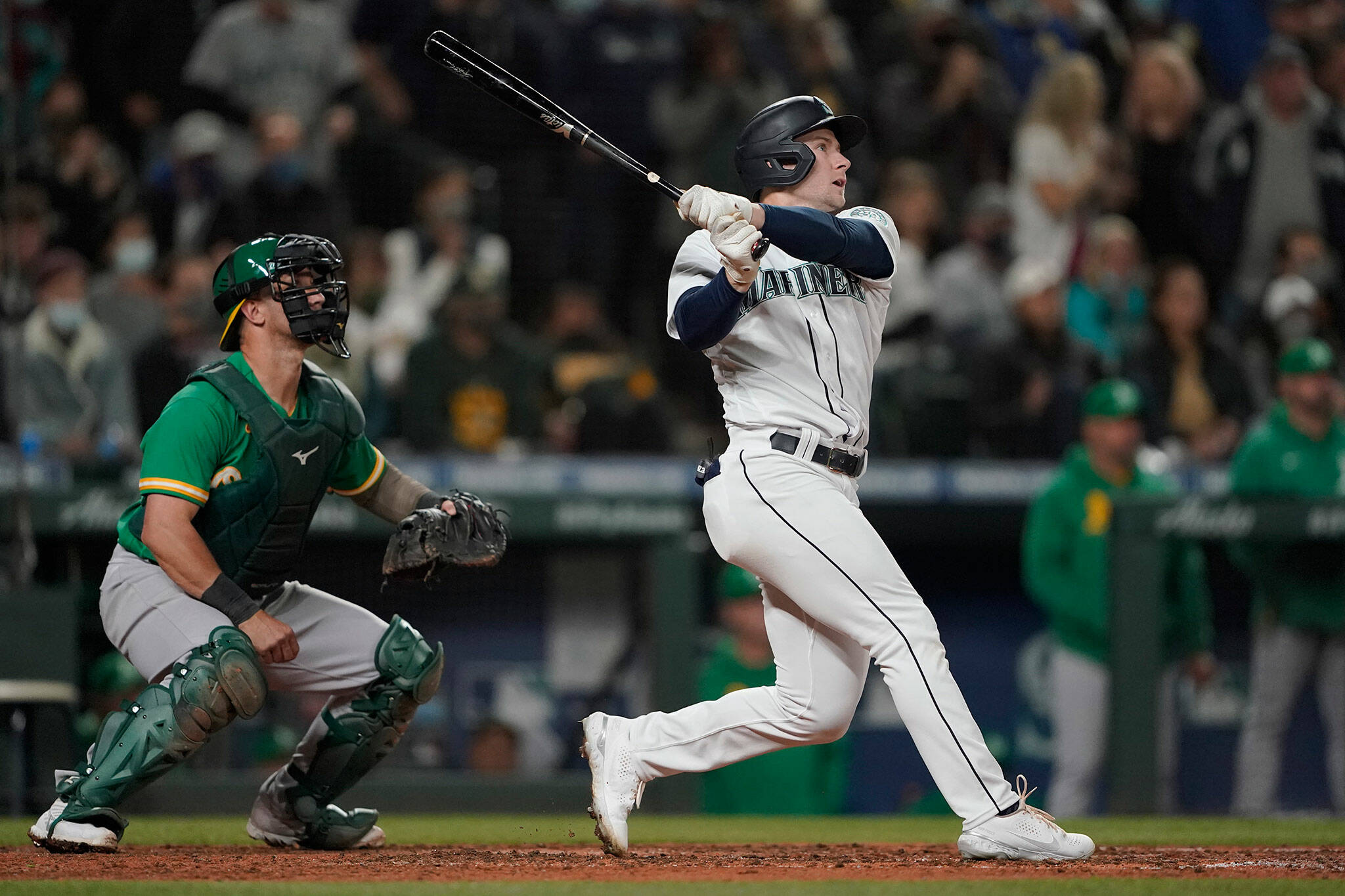 The Mariners’ Jarred Kelenic follows through on a two-RBI double as Athletics catcher Yan Gomes looks on during the sixth inning of a game Wednesday in Seattle. Mitch Haniger and Ty France scored on the play. (AP Photo/Ted S. Warren)