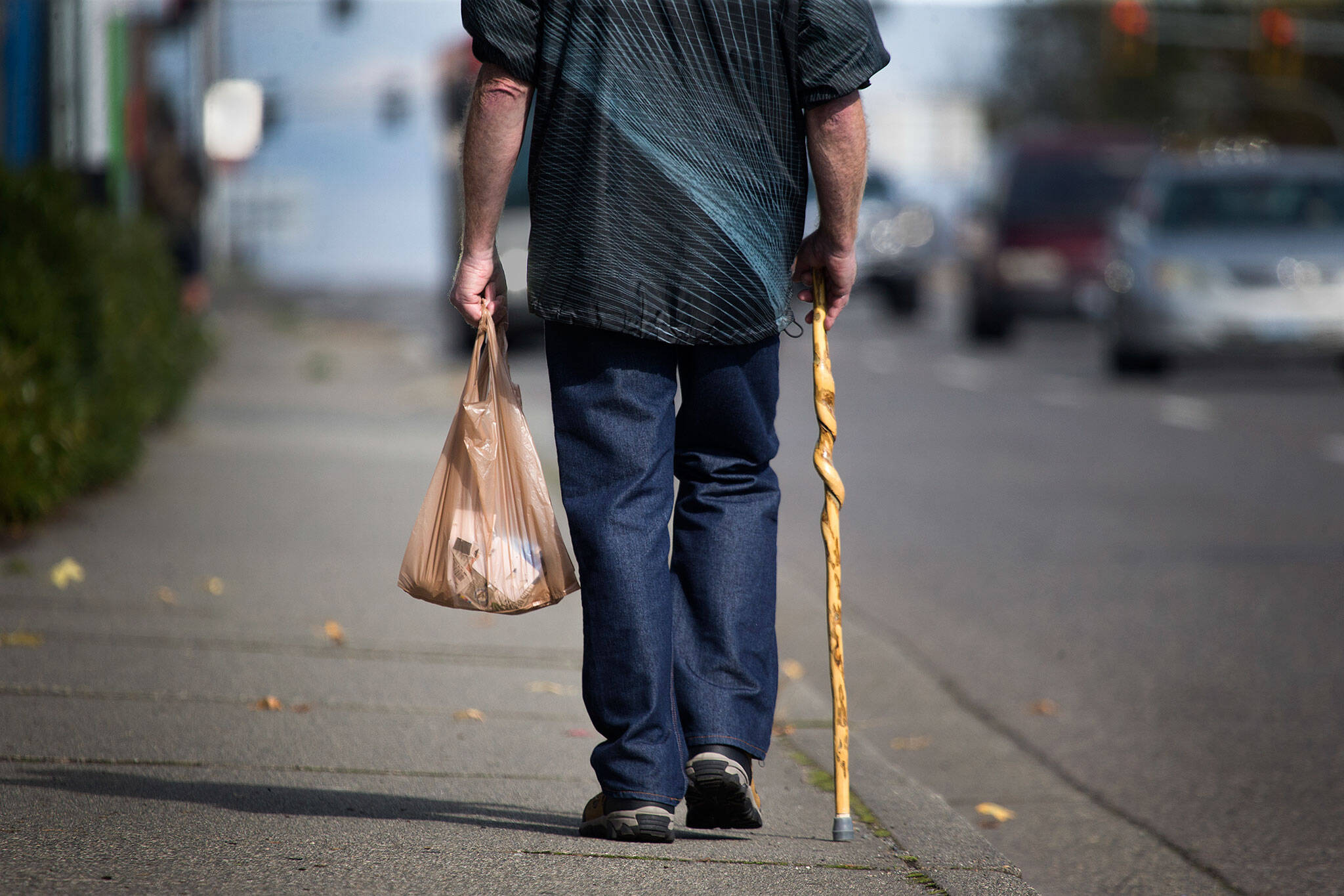 A man carries items in a plastic bag as he walks own Evergreen Way in 2018 in Everett. (Andy Bronson / Herald file)