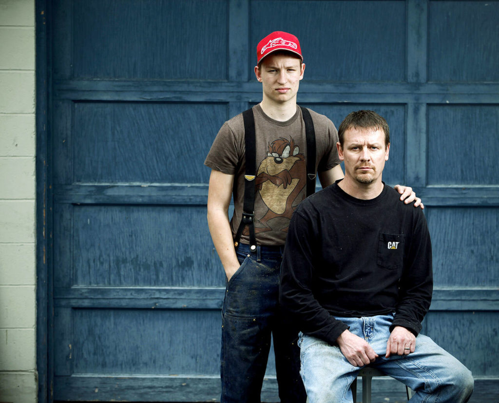 Dayn Brunner and his son Riley (age 17 at the time) pose for a photo at Darrington High School on March 12, 2015. Dayn’s sister, Summer Raffo, was one of the 43 victims of the Oso mudslide. Dayn and Riley spent five days searching the debris field before finding Summer in her car, hands still on the steering wheel. Dayn spent a total of 39 days searching through the mud for other victims. (Genna Martin / Herald file)
