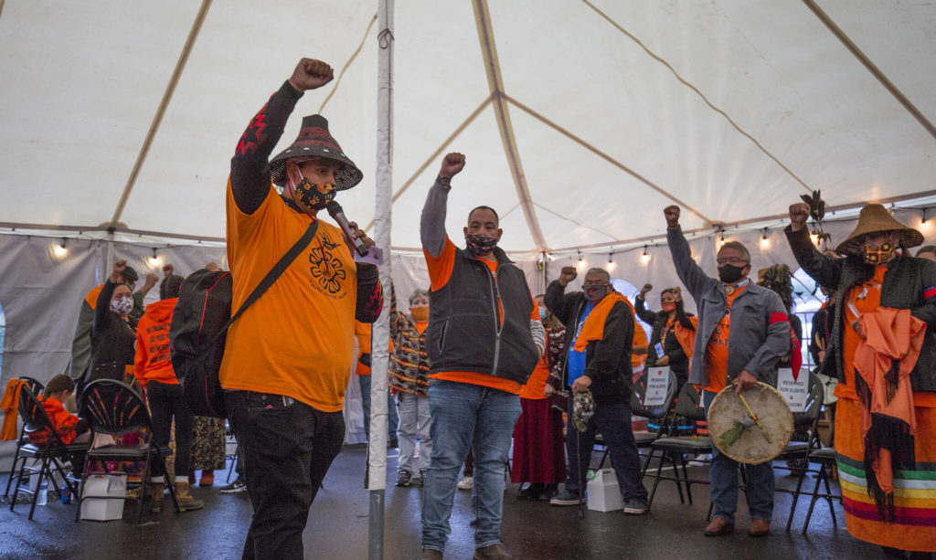 The Tulalip Tribes community members raise a fist as they gather at the last remaining building from the Tulalip Indian boarding school for a Day of Remembrance on Thursday in Tulalip Reservation. The Tulalip Tribes passed a resolution proclaiming Sept. 30 as Orange Shirt Day, a day of remembrance and awareness for Residential Boarding Schools. (Andy Bronson / The Herald)
