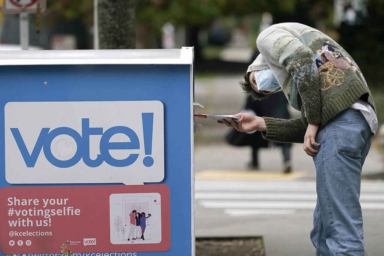 A voter turns sideways as he eyes the opening of a ballot drop box before placing his ballot inside it in Seattle in October 2020. (Elaine Thompson / Associated Press file photo)