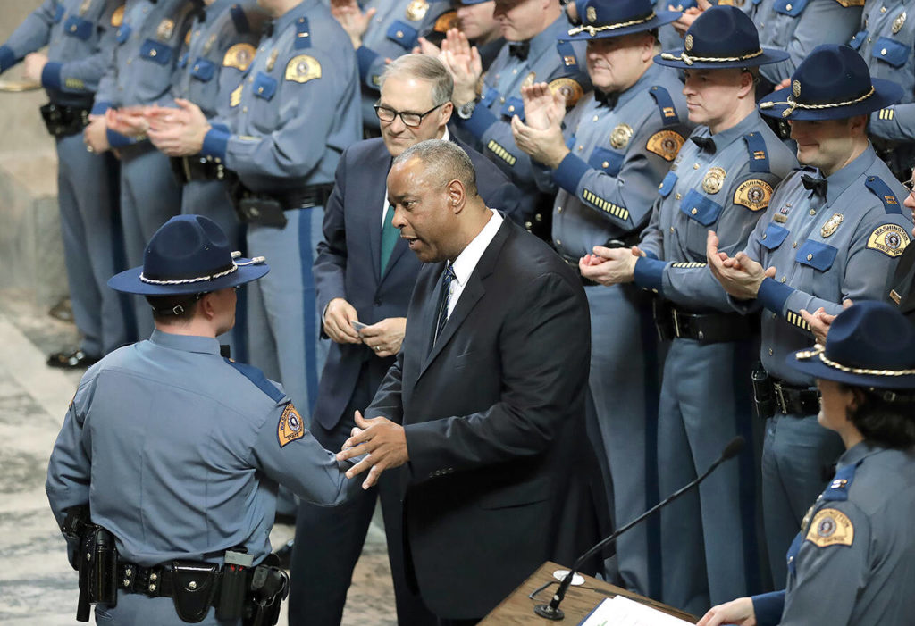 The Washington State Patrol lost 127 employees who missed the deadline to prove they were vaccinated against COVID-19 or had an exemption and accommodation to keep working. Here, in this December 2018 photo, WSP Chief John Batiste (center) greets a new trooper during a graduation ceremony, as Gov. Jay Inslee looks on in the Rotunda at the Capitol in Olympia. (AP Photo/Ted S. Warren, file)
