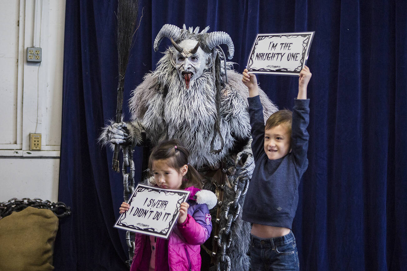Samantha Breeden, 3, left, and brother John Breeden, 5, right, pose for a photo with Krampus at Oddmall: Emporium of the Weird on Nov. 9, 2019 in Monroe, Wash. (Olivia Vanni / The Herald)