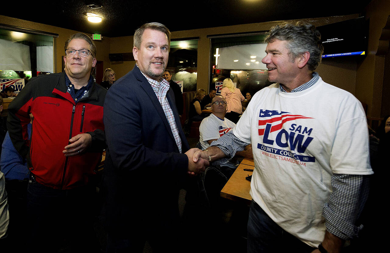 Snohomish County Councilman Sam Low (center) is congratulated by Snohomish Regional Fire and Rescue Fire Chief Kevin O’Brien (right) as results show Low in the lead during an election night party at Nachos Family Mexican Restaurant on Tuesday in Lake Stevens. (Andy Bronson / The Herald)