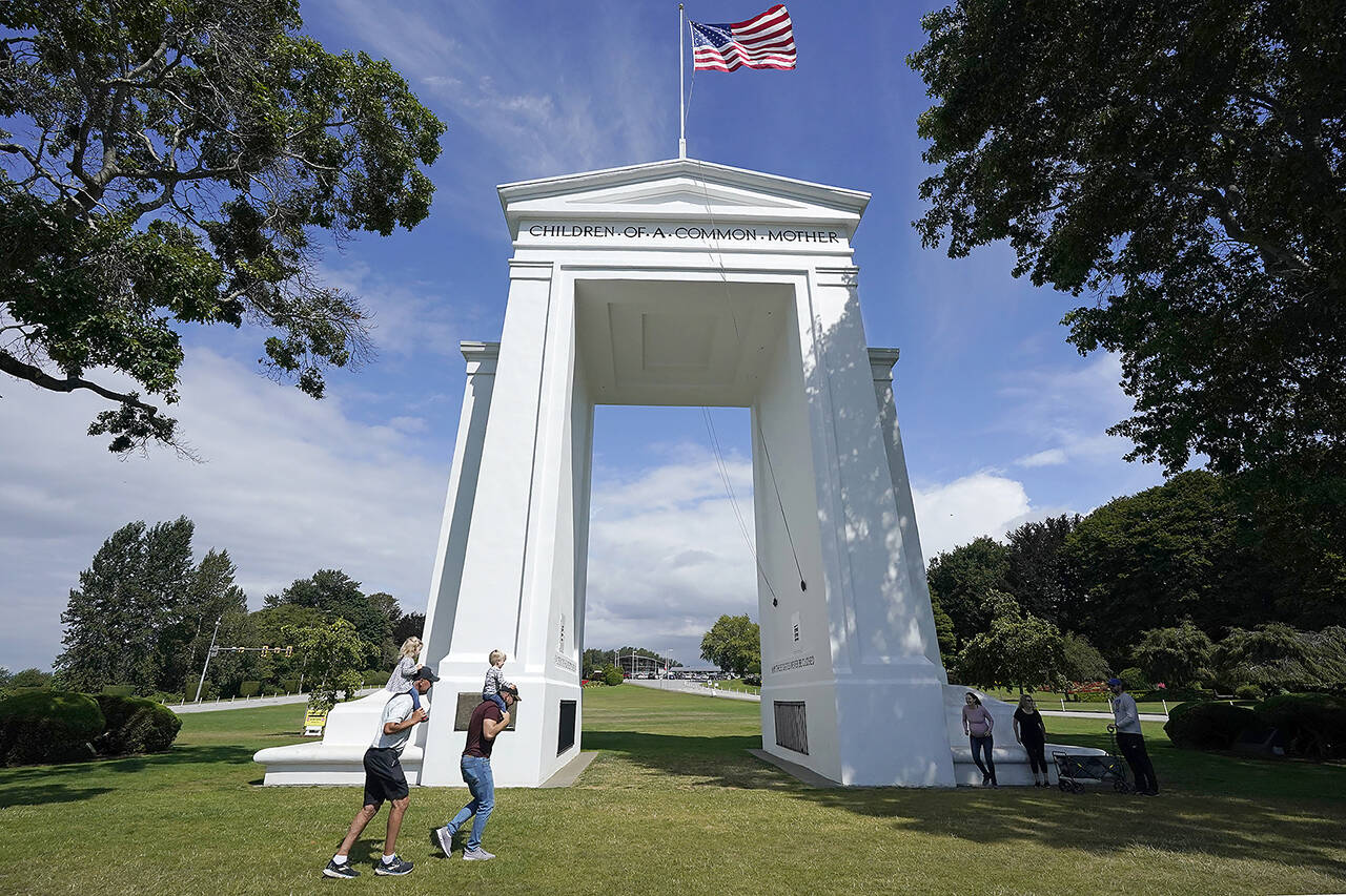 People walk adjacent to the border with Canada at the Peace Arch in Peace Arch Historical State Park, where cars behind wait to enter Canada at the border crossing Aug. 9 in Blaine. (AP Photo/Elaine Thompson, file)