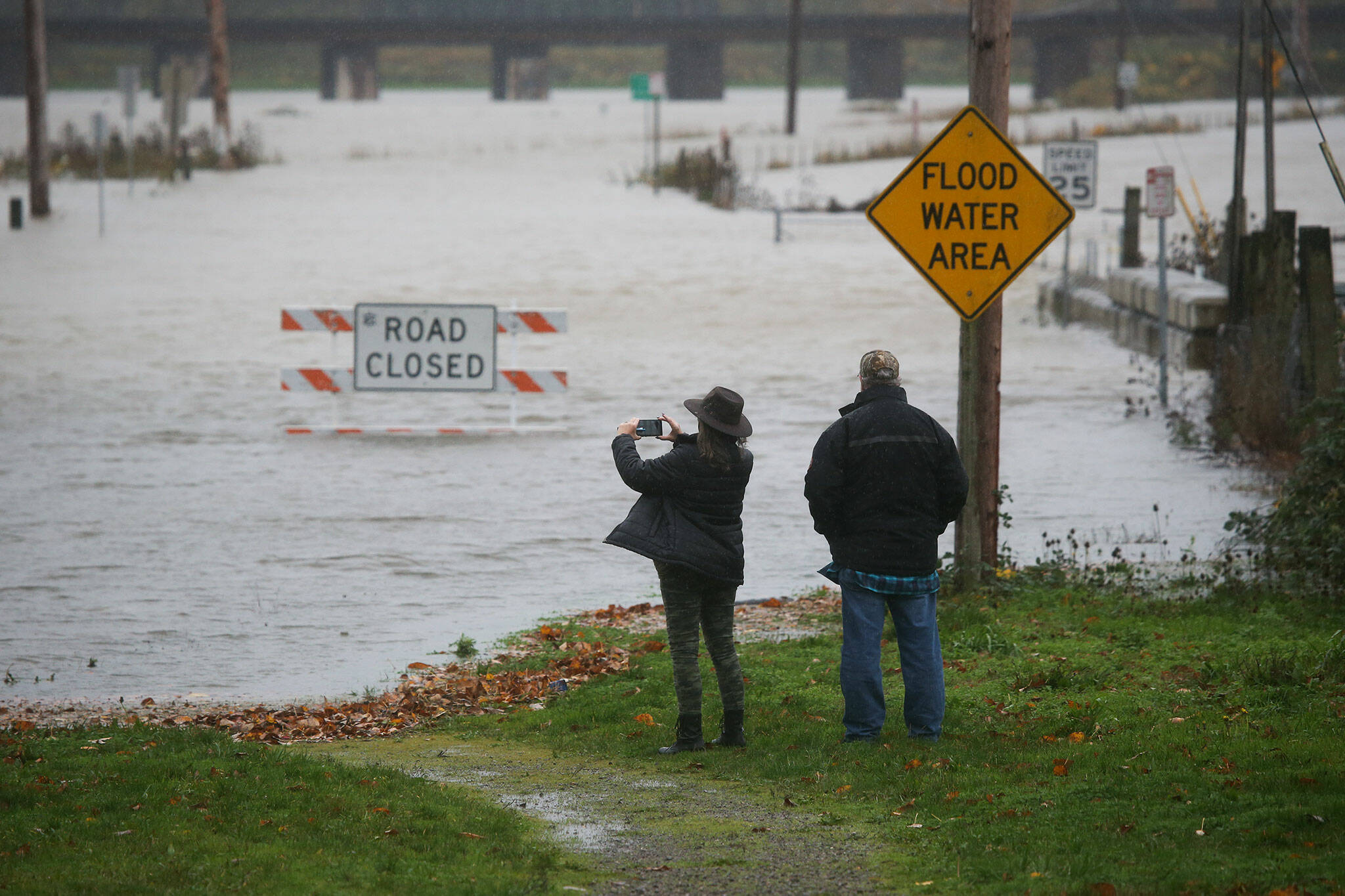 Pam and Ken Owens, of Granite Falls, stop to take cellphone photos of the flooding along Lincoln Avenue on Monday in Snohomish. The couple were planing to take the road to Monroe for lunch. (Andy Bronson / The Herald)