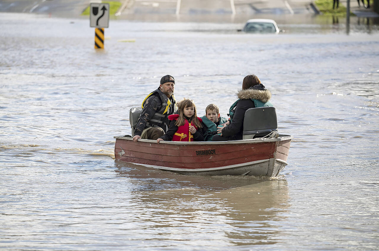 A woman and children who were stranded by high water due to flooding are rescued by a volunteer operating a boat in Abbotsford, British Columbia on Tuesday. (Darryl Dyck/The Canadian Press via AP)