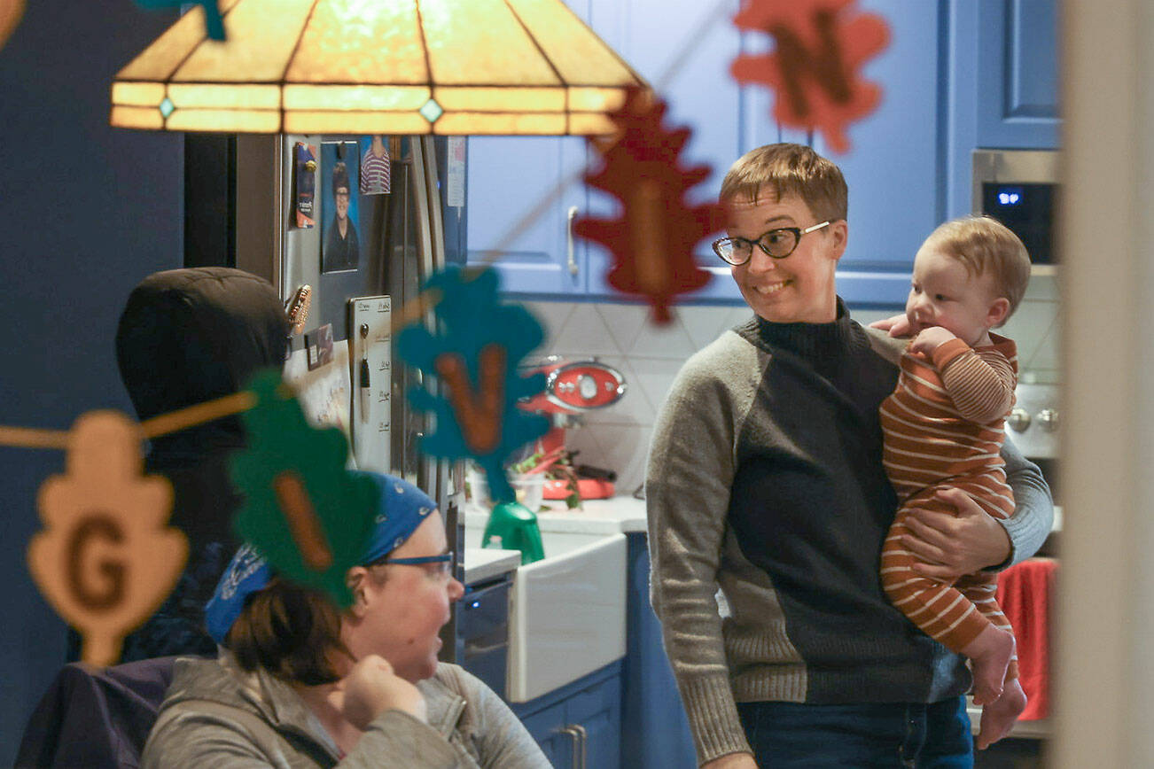 Holding her nine-month-old son Oliver,  Kate Torrey talks with older son Isaac and partner Lindsay, in their kitchen  at their home on Saturday, Jan. 1, 2021 in Snohomish, Washington. Like many families last year, The Torreys skipped out on the usual Thanksgiving get-together. This year will be the first time some family members get to meet her new baby. (Andy Bronson / The Herald)