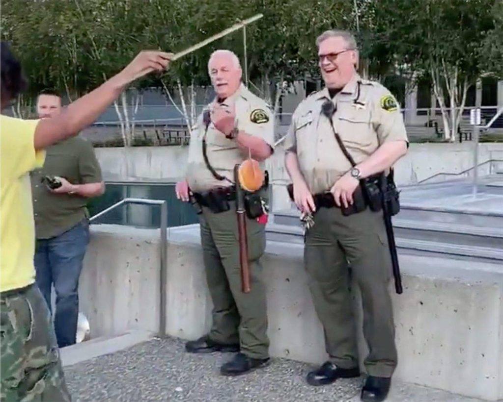 Benjamin Hansen dangles a doughnut in front of two law enforcement officers in Everett in July 2020. (Screen grab from video courtesy of Bennett Haselton) 
