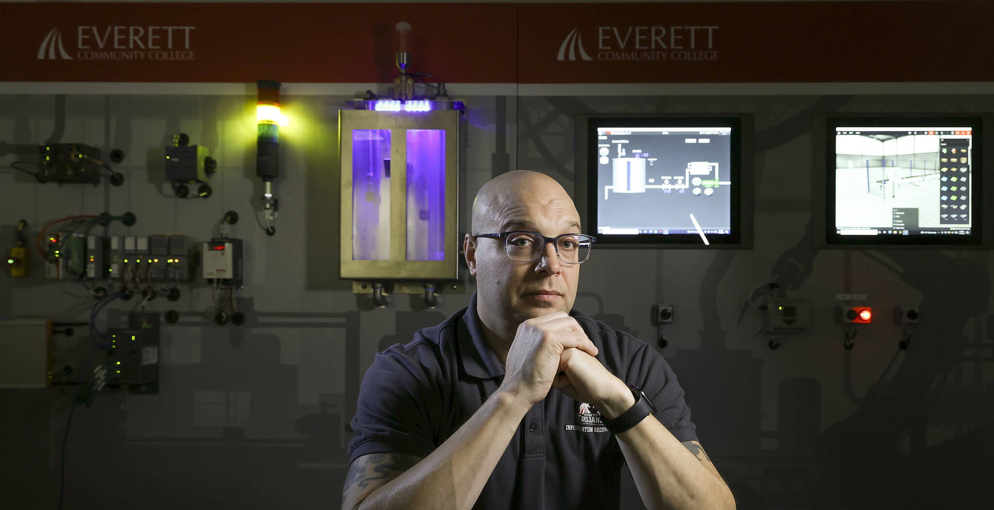 Everett Community College’s Dennis Skarr sits in front of a 15-foot interactive wall that can replicate a manufacturing company’s assembly line, hardware, software and networks. (Andy Bronson / The Herald)