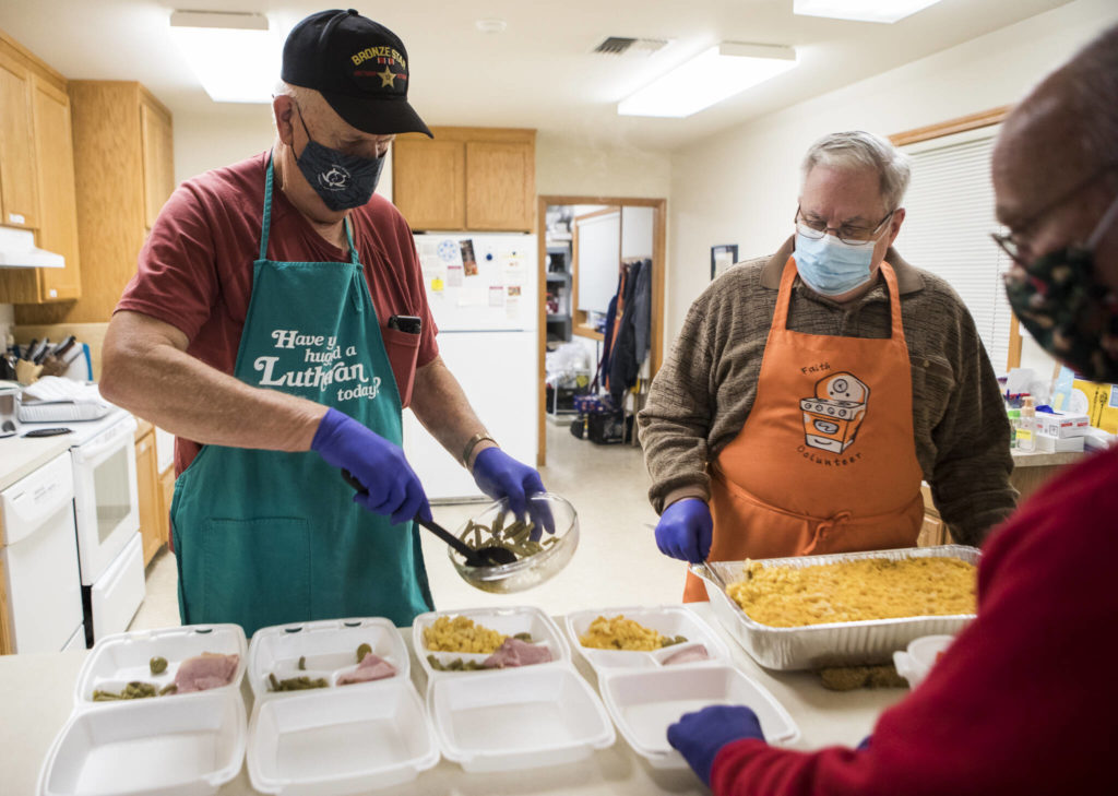 Mike Larson (left) puts together to-go meals with the help of Paul Rode (center) and Roger Chester (right) during Faith Lutheran Church’s hot meal night Nov. 30 in Everett. The church is part of the Everett Hot Meals Coalition, a group of 12 organizations that coordinate meal service across the city. (Olivia Vanni / The Herald)
