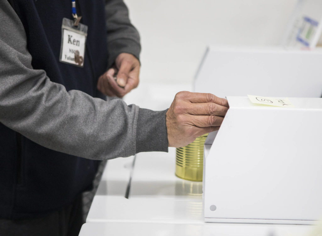 A volunteer places quarters in a washing machine during North Snohomish County Laundry Outreach on Dec. 1 in Arlington. (Olivia Vanni / The Herald)
