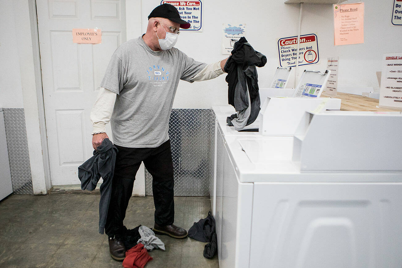 Hank Henry places a load of laundry in a washing machine at Suds & Duds Laundry during North Snohomish County Laundry Outreach on Wednesday, Dec. 1, 2021 in Arlington, Wa. (Olivia Vanni / The Herald)