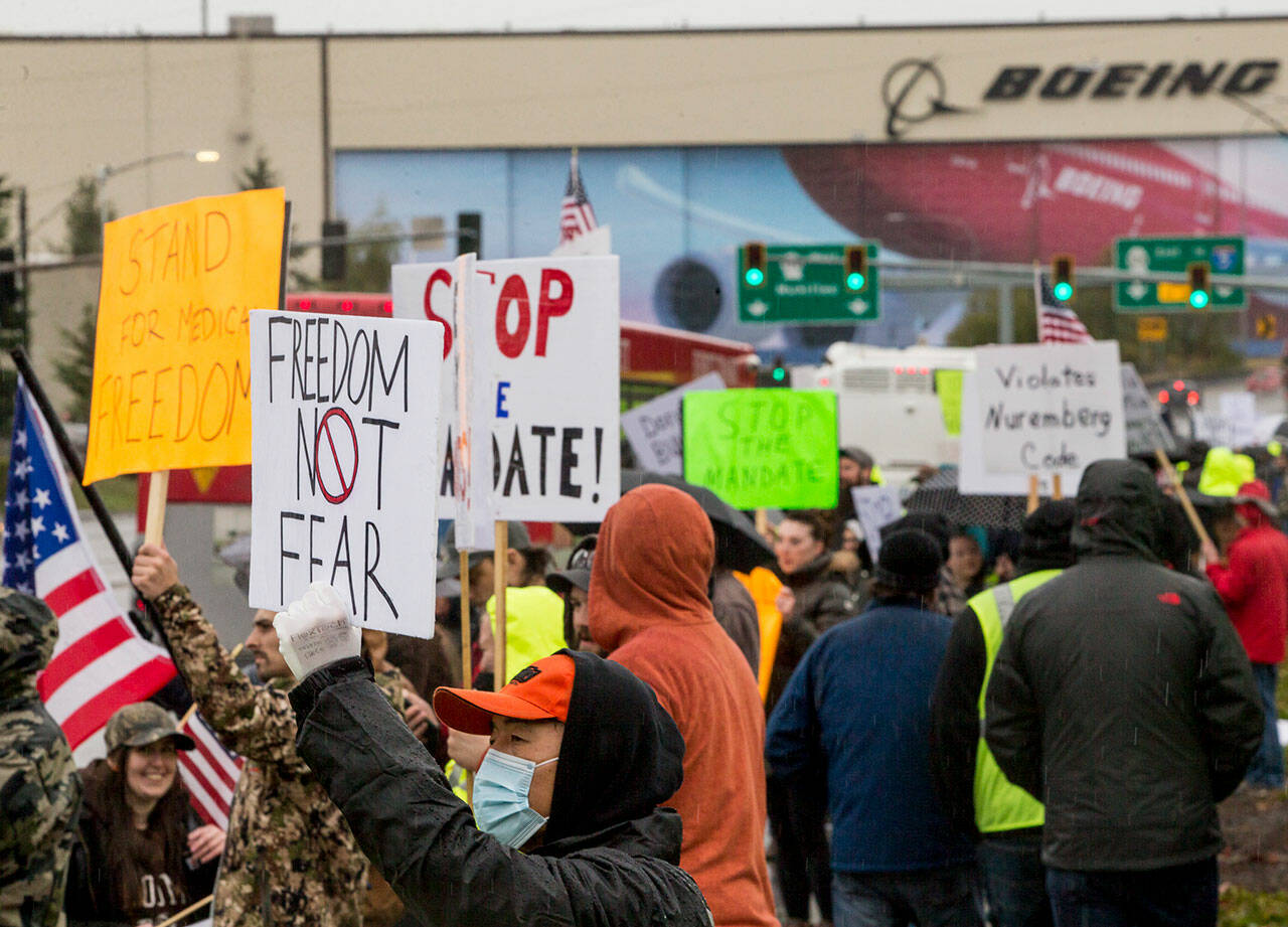 People hold signs in protest of the vaccine mandate last month in Everett, after Boeing announced it would terminate workers who do not comply. (Olivia Vanni / Herald file)