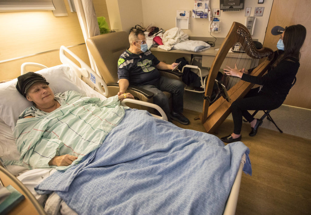 Shelly Holmgren (left) holds hands with her brother Jay Holmgren (center) while they listen to music thanatologist April Mitchell play the harp at Providence Regional Medical Center Everett on Dec. 17, 2021. (Olivia Vanni / The Herald)
