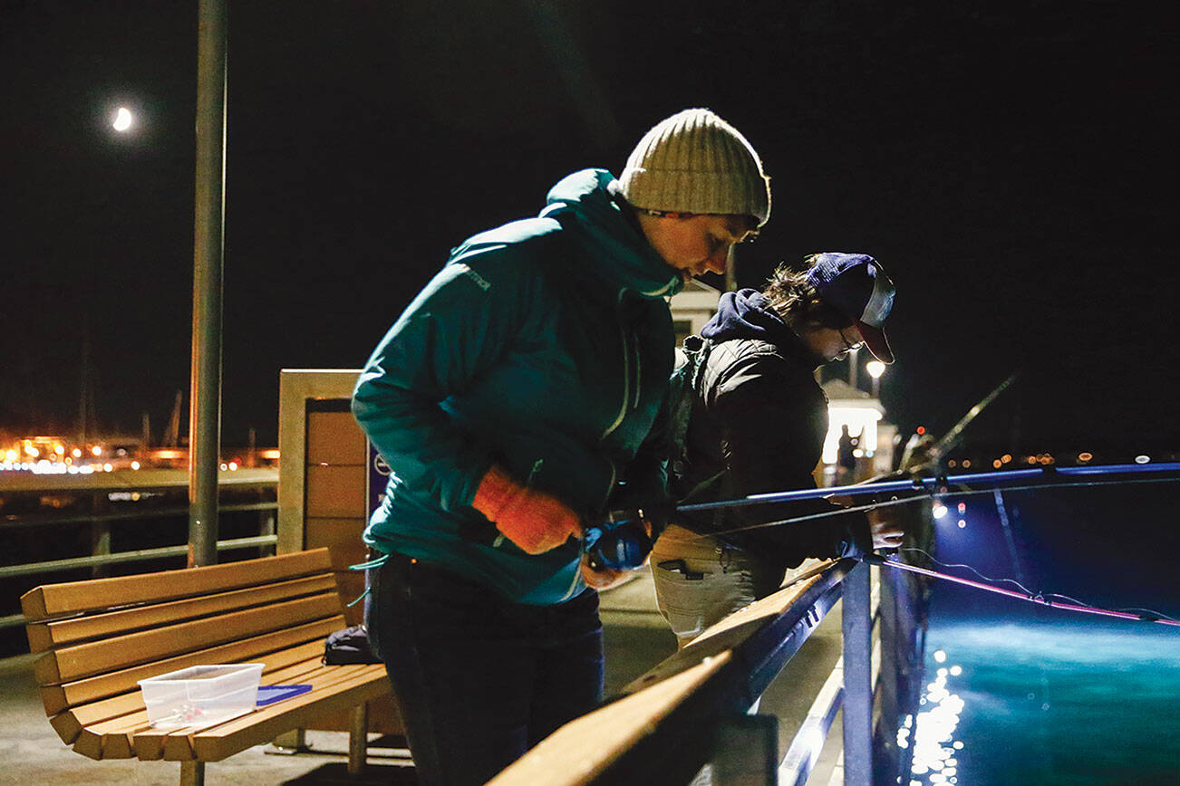 Lauren VanderLugt and Vienna Wong cast lines for squid Monday night on the Edmonds Fishing Pier on October 11, 2021.  (Kevin Clark / The Herald)