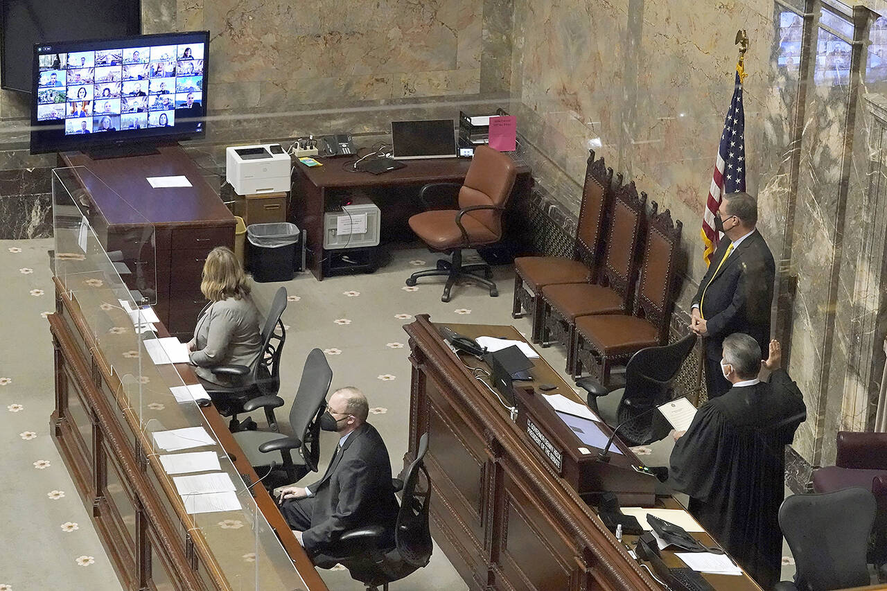 Washington state Supreme Court Chief Justice Steven C. Gonzalez (bottom right) looks at a remote video meeting screen as he swears in Sen. John Lovick, D-Mill Creek, as vice president pro tempore of the Senate on Monday at the Capitol in Olympia. Lovick had to be sworn in remotely because he tested positive for COVID-19 last week. (AP Photo/Ted S. Warren)