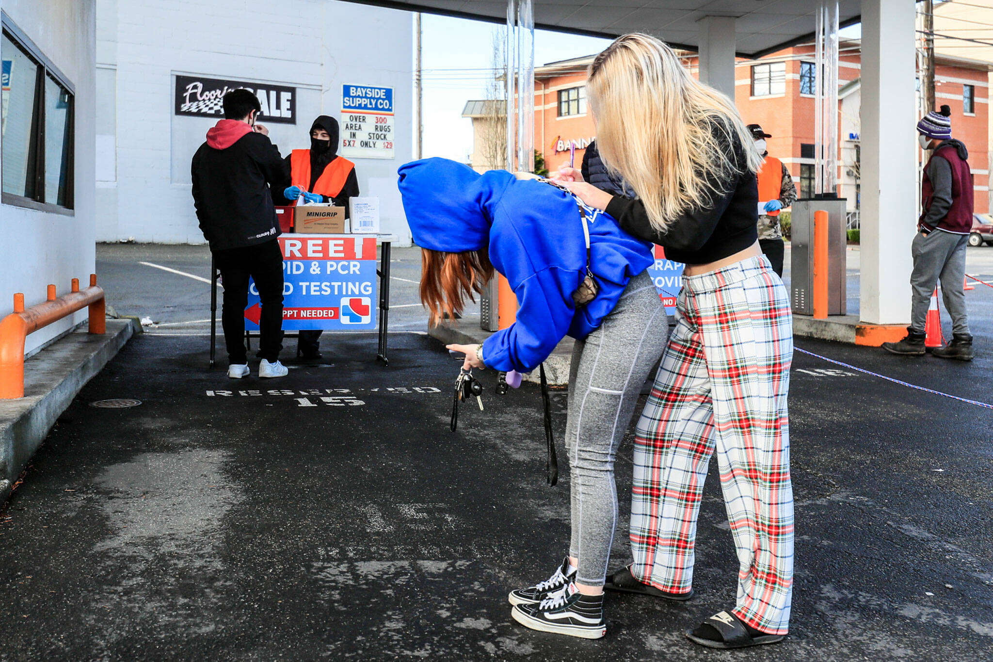 Sam Dawson (right) fills out a registration card with the help of her friend, Shay Daniels, on Thursday at the walk-up COVID testing center on Wetmore Avenue in Everett. (Kevin Clark / The Herald)