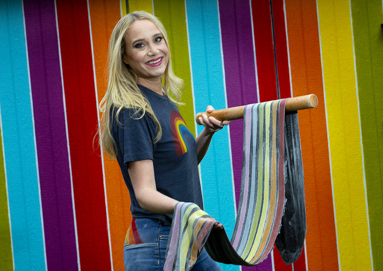 Linda Miller Nicholson, of Fall City, holds up rainbow pasta she just made in the commercial kitchen at her home. The rainbow wall behind her is in her back yard. (Ellen M. Banner / The Seattle Times)