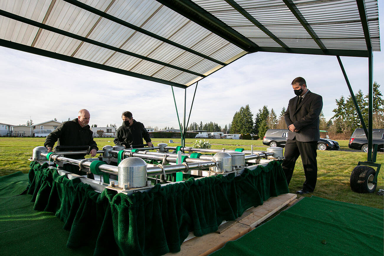 Chris Amundson, right, watches as the caskets of his granddaughters Adriana and Mariel Gil are lowered into their graves Friday, Jan. 28, 2022, at Cypress Lawn Memorial Park in Everett, Washington. (Ryan Berry / The Herald)