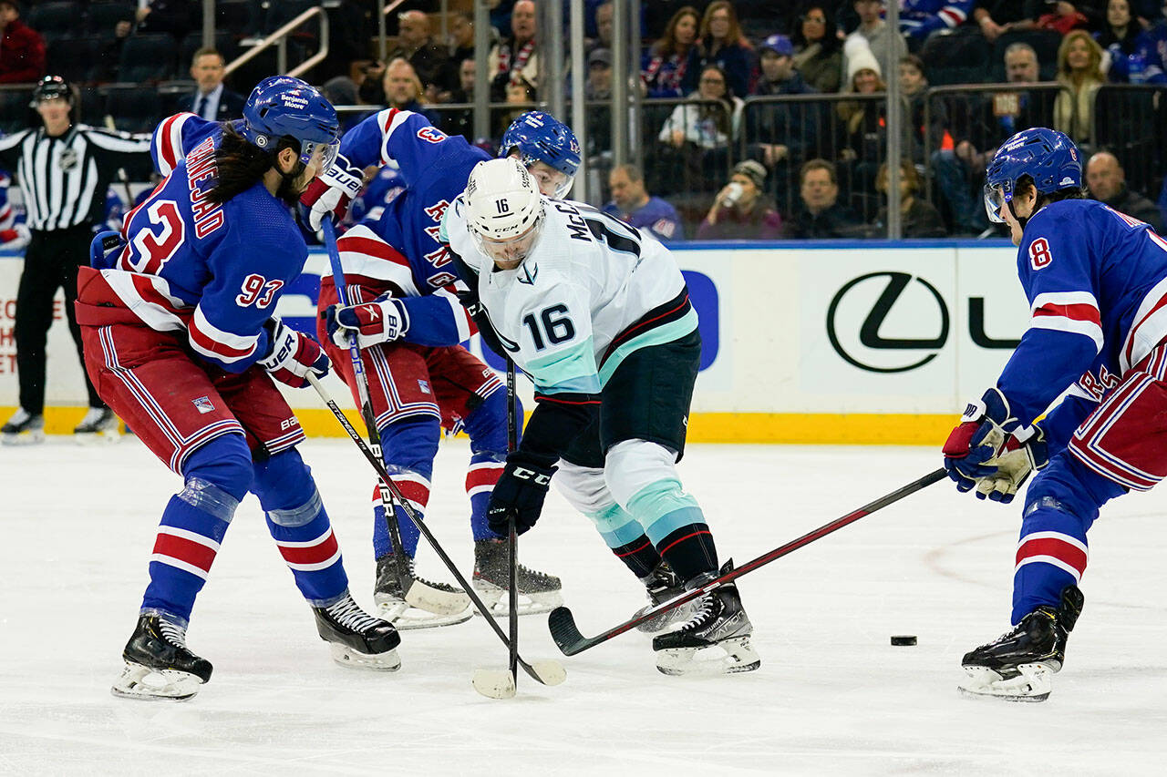 Seattle Kraken left wing Jared McCann (16) is triple-teamed by New York Rangers center Mika Zibanejad (93), left wing Alexis Lafrenière (13), and defenseman Jacob Trouba (8) during the first period of a game, Sunday, Jan. 30, 2022, in New York. (AP Photo/John Minchillo)
