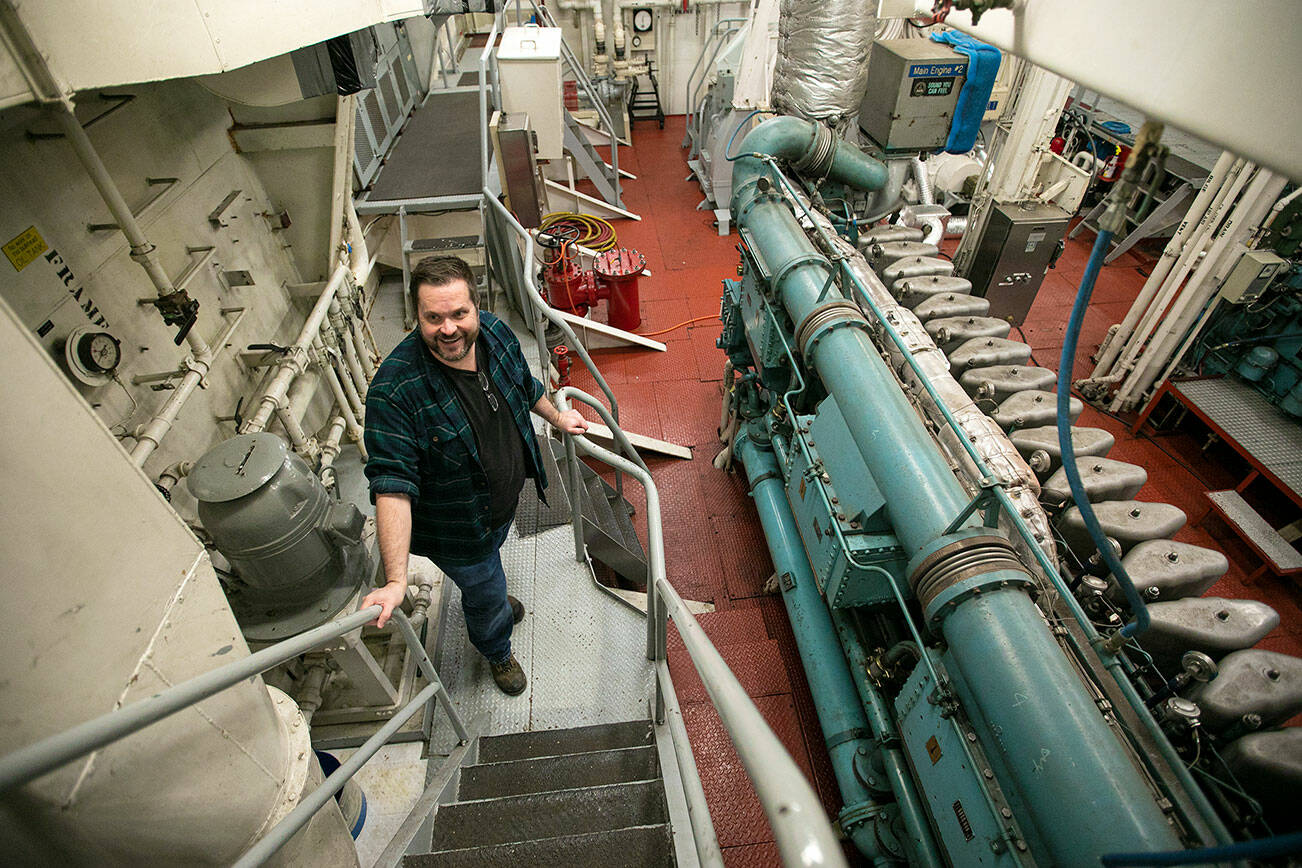 Bart Lematta proudly stands in the engine room of his ferry Tuesday, Feb. 8, 2022, along the shore of Langley, Washington. “I go down in the engine room, picture all the work that has gone into it and all the hands, the artistry and craftsmen,” he said. “It’s a beautiful piece of artwork that has taken millions of hours.” (Ryan Berry / The Herald)