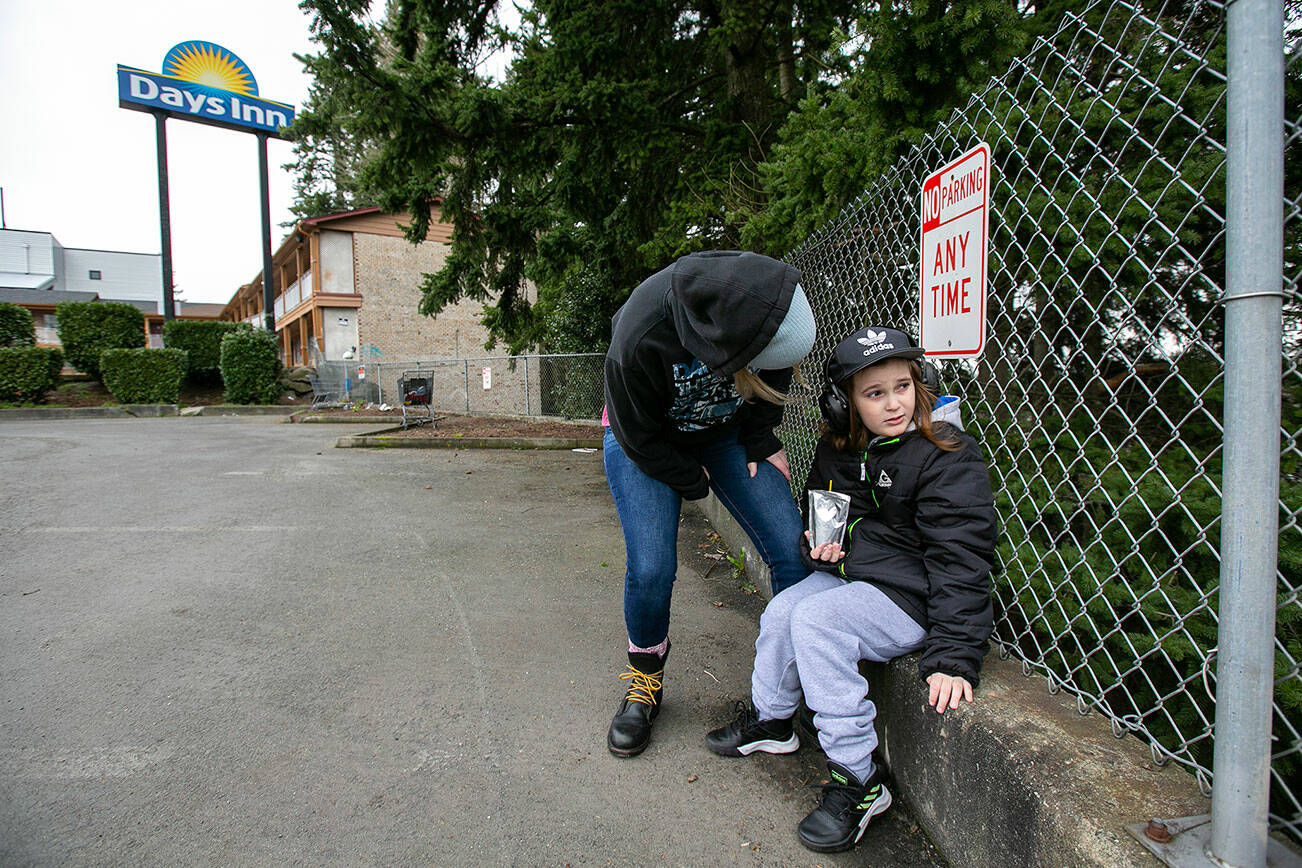 Melinda Parke and her 8-year-old son Elijah sit outside and watch cars pass by on the freeway outside their motel at the Days Inn Friday, Feb. 11, 2022, in Everett, Washington. Melinda said watching the cars is a daily routine that helps keep Elijah, who is autistic, stay calm during the family’s time without a home. (Ryan Berry / The Herald)