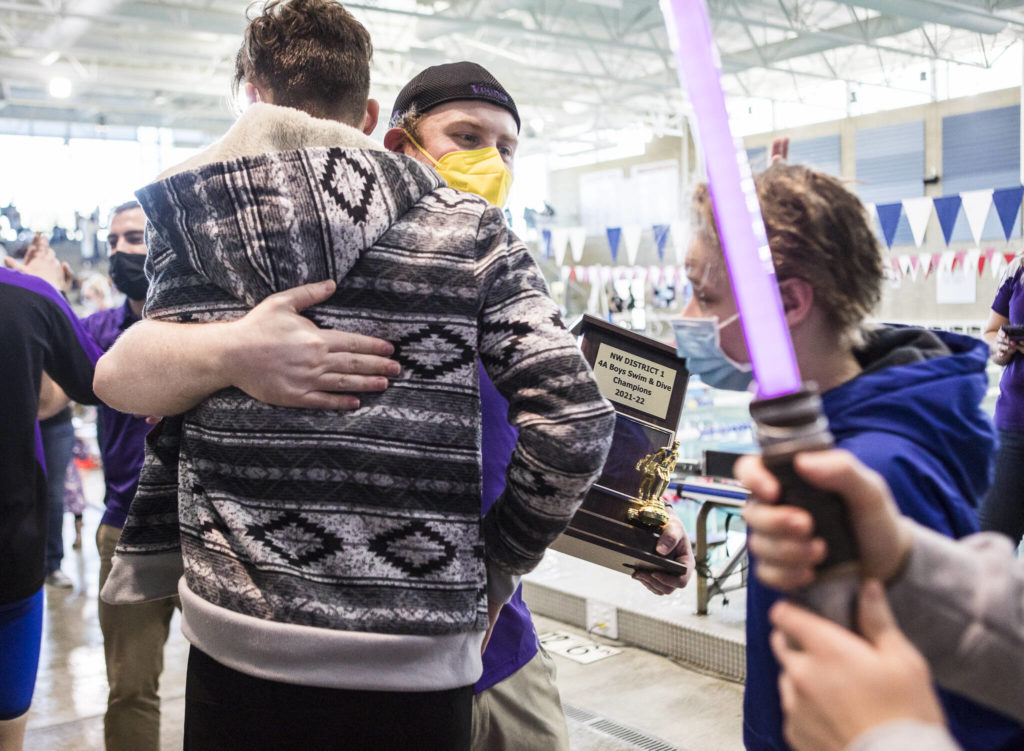Lake Stevens head coach Brady Dykgraaf hugs his swimmers while holding the NW District 1 4A Boys Swim & Dive championship trophy after winning the 4A Boys Districts swim meet on Saturday, Feb. 12, 2022 in Snohomish, Wa. (Olivia Vanni / The Herald)
