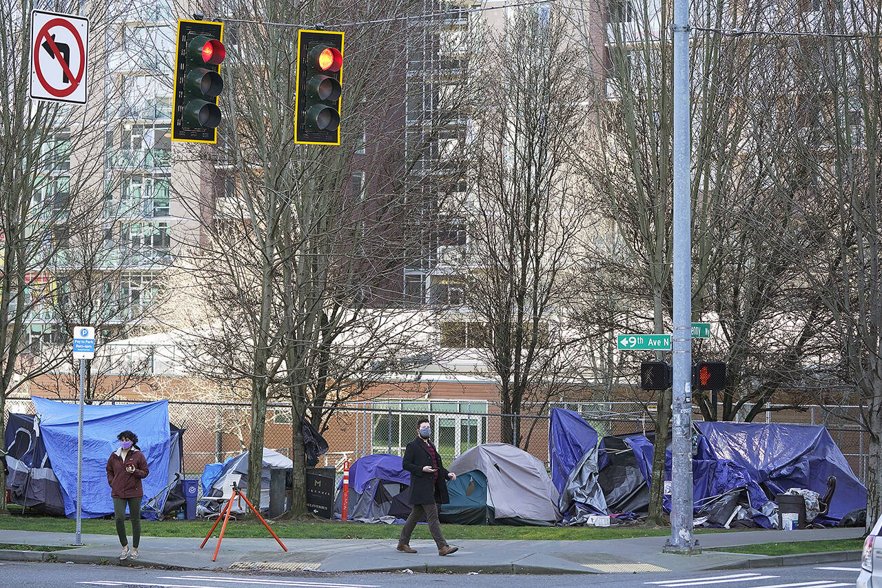 In this 2021 photo, pedestrians walk past tents used by people lacking housing at Denny Park near the Space Needle in Seattle. (AP Photo/Ted S. Warren, File)